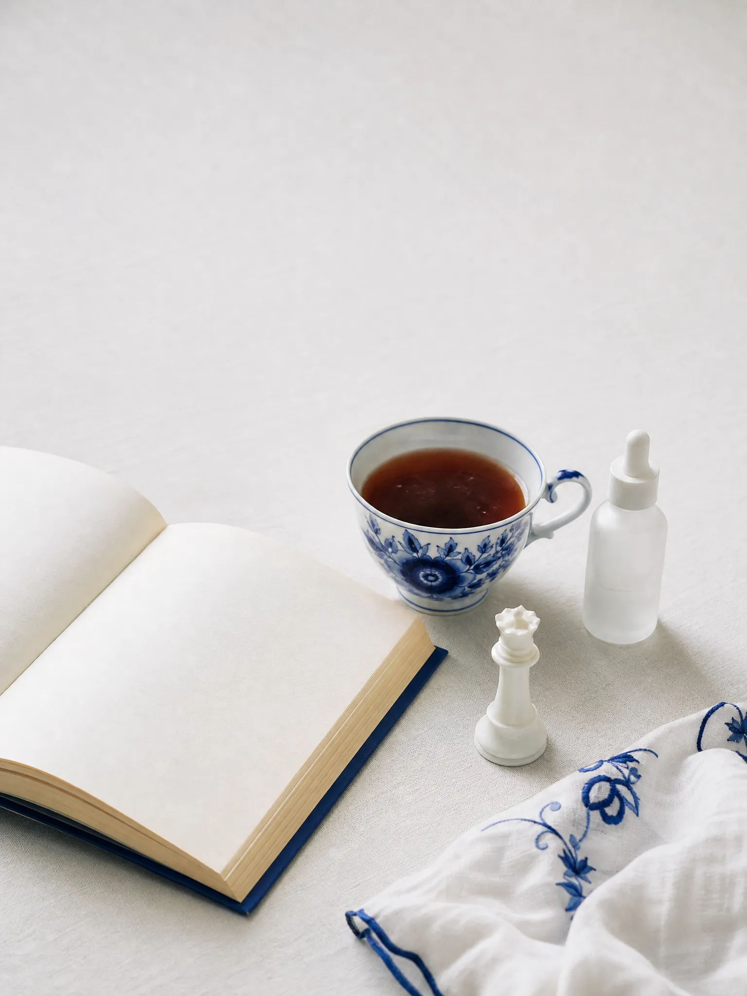 Tea in a Gzhel cup beside an open book, a serum bottle and a chess queen
